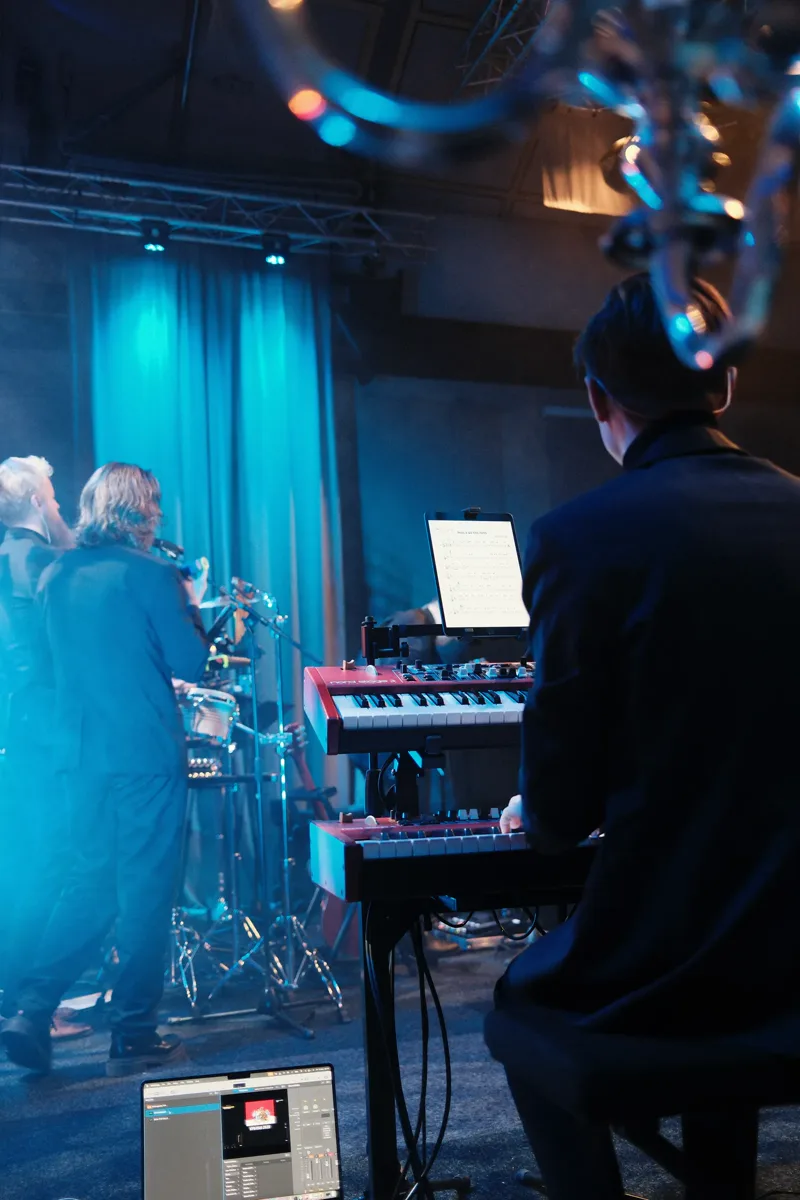Pianist på scen med blått ljus och musiker bakom